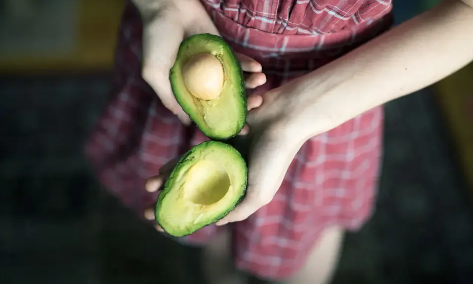 Hände halten eine aufgeschnittene Avocado, bereit für eine pflegende Avocado-Maske für die Haare.