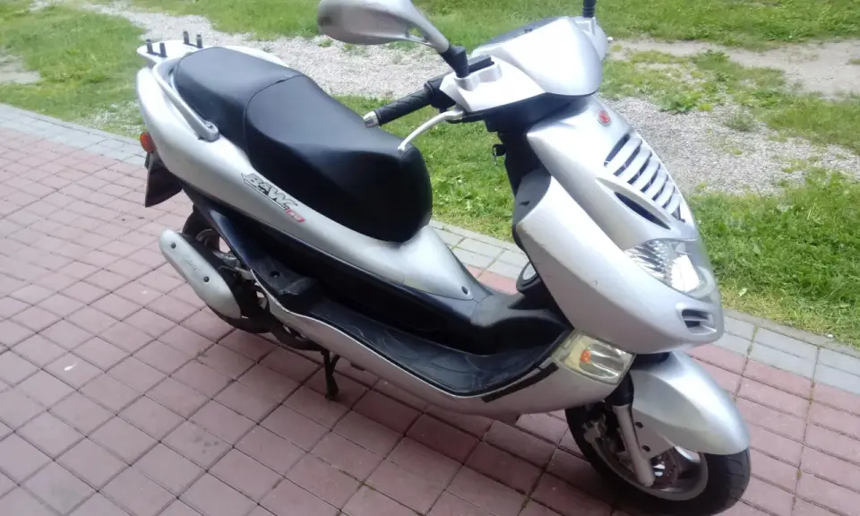 Srebrny skuter Kymco Bet&Win 50 stoi na chodniku z kostki brukowej.