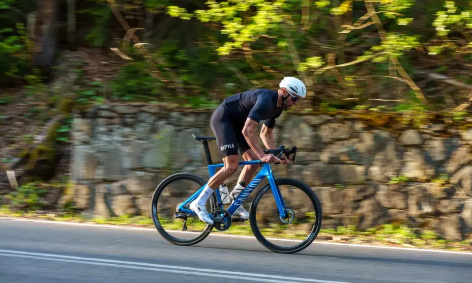 Kolarz w kasku ściga się na niebieskim rowerze Canyon Endurace CF 7 po malowniczej drodze wśród zieleni.