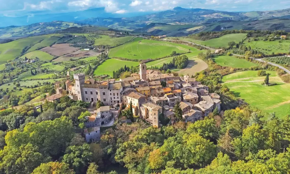 Un borgo medievale arroccato su una collina, circondato da dolci colline verdi. Un esempio dei borghi più belli della Toscana.