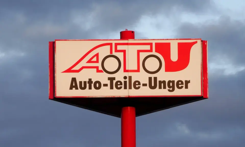 Schild mit rotem Schriftzug "A.T.U. Auto-Teile-Unger" vor bewölktem Himmel.