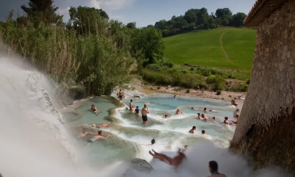 Persone si rilassano nelle cascate naturali delle **Terme di Saturnia**, immerse nel verde della campagna toscana.
