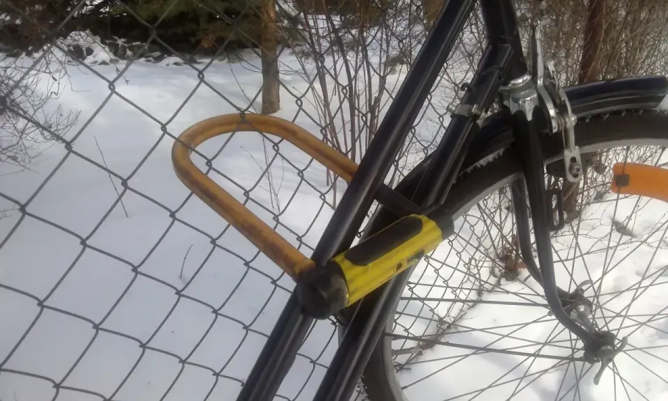 Żółta kłódka U-lock zabezpieczenie roweru przed kradzieżą, przypiętego do siatki w zimowy dzień.