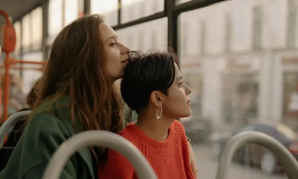 Two women share a tender moment on a bus, perhaps on their gay honeymoon, gazing out the window at the passing scenery.