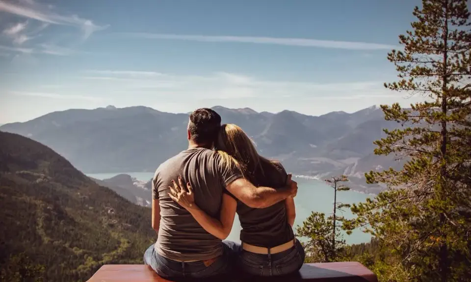 Un couple partage un moment d'amour sensuel, bras dessus, bras dessous, contemplant un paysage montagneux et un lac paisible.