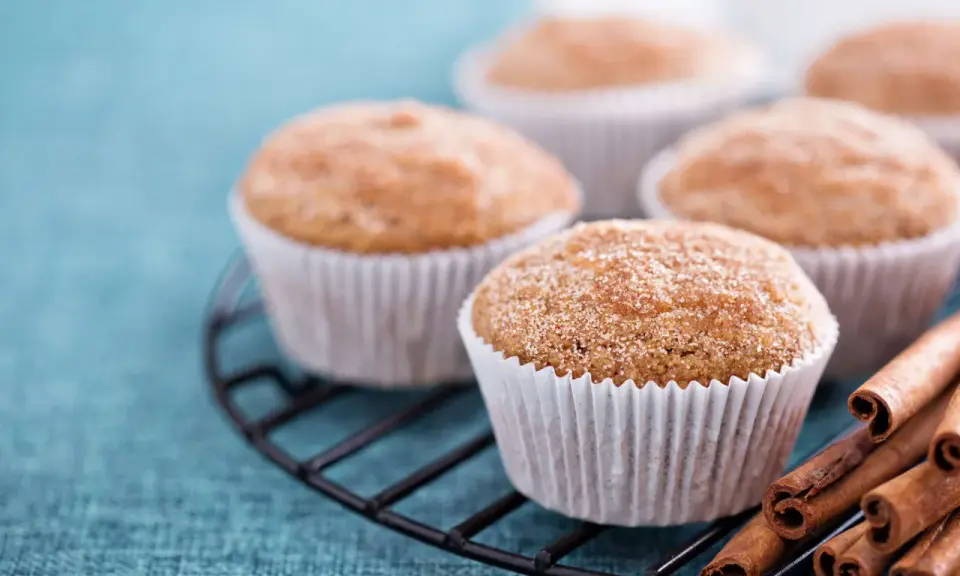 Leckere Apfelmus Muffins mit Zimt bestreut auf einem Gitter, daneben Zimtstangen.