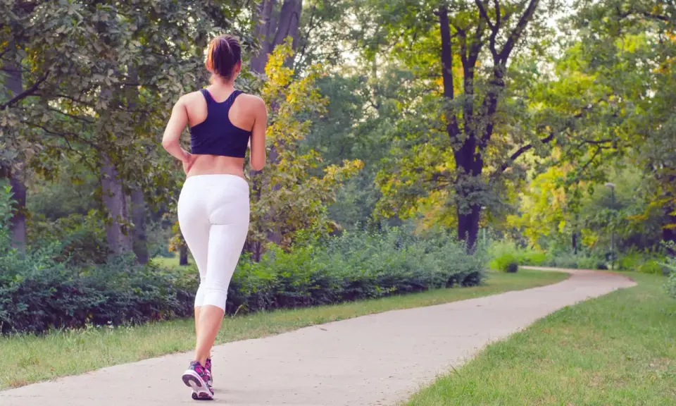 Donna corre su un sentiero nel parco, godendosi la sua zona 2 corsa tra gli alberi verdi.
