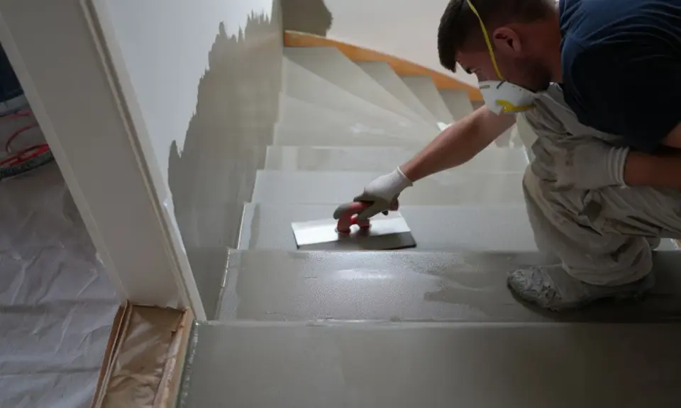 Un ouvrier, masqué et ganté, applique un enduit sur les marches d'un escalier en cours de restauration.