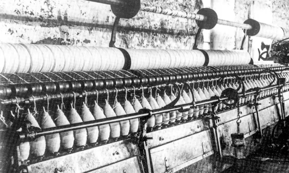 Macchinario industriale per la filatura con fili avvolti su bobine e grandi rulli.