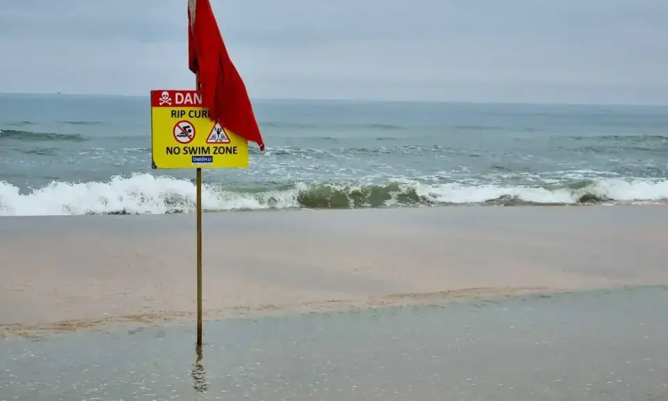 Röd flagga och skylt varnar för farliga strömmar vid stranden i Goa, Indien. Ingen badzon.