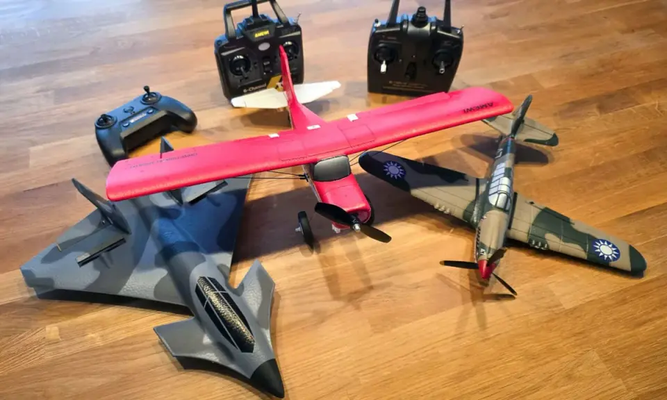 Mehrere ferngesteuerte Flugzeuge, darunter ein rotes Kunstflugmodell und ein Tarnkappenbomber, liegen bereit, um abzuheben.