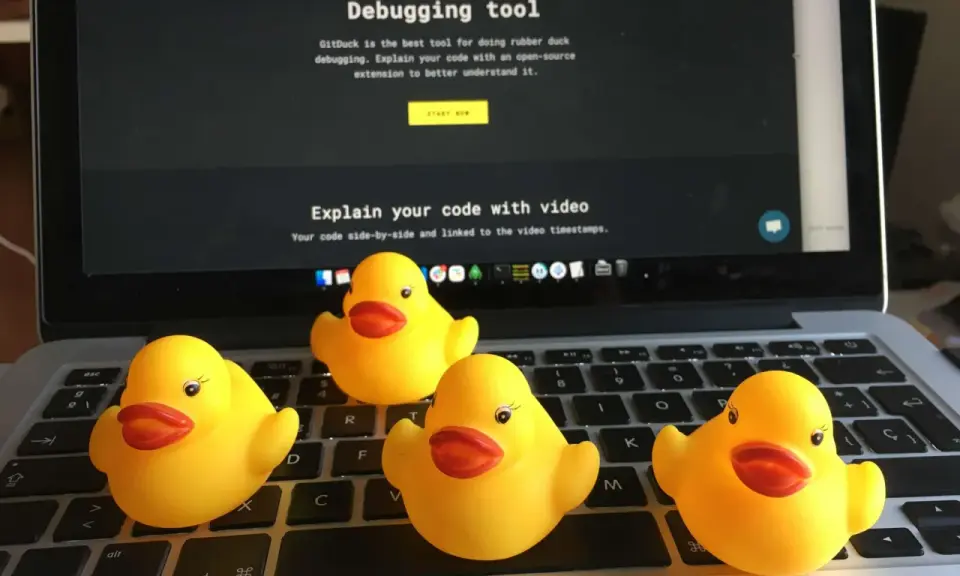 Cztery żółte gumowe kaczuszki siedzą na klawiaturze laptopa, obok ekranu z napisem "The Rubber Duck Debugging tool".