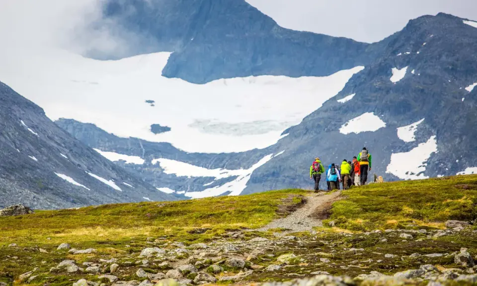 Vandrare med ryggsäckar går längs en stig med glaciärklädda sylarna runt.