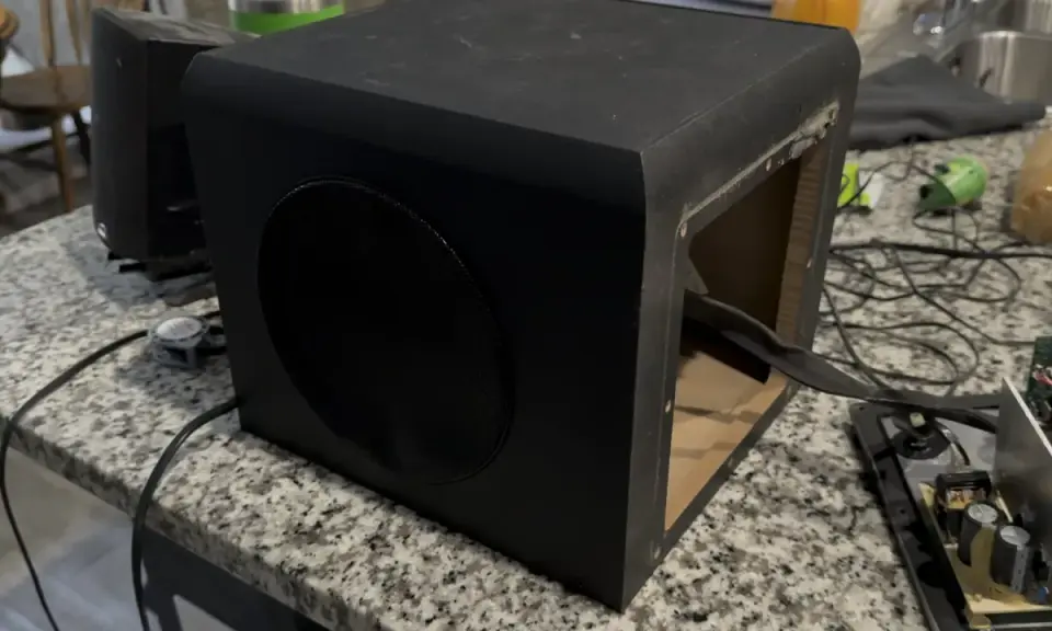 Un caisson de basse noir ouvert sur une table. Pour savoir si un caisson de basse fonctionne, vérifiez les connexions et le circuit imprimé.
