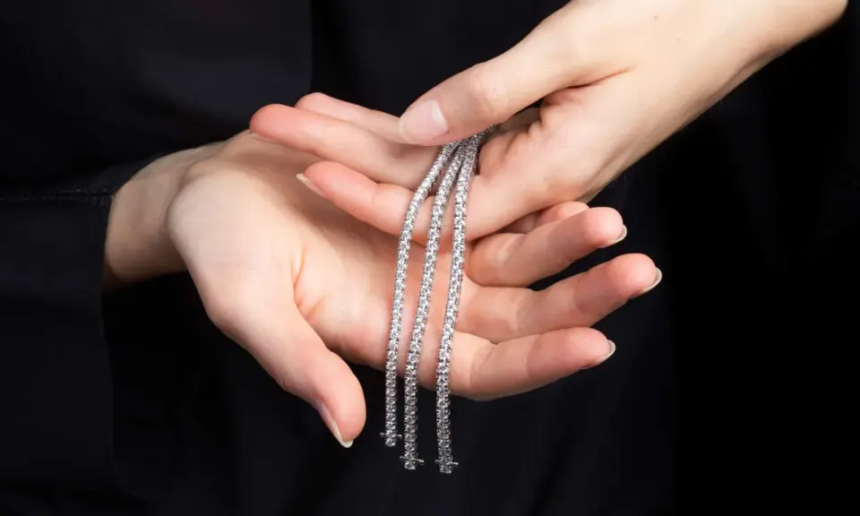 Mani delicate tengono tre scintillanti bracciali tennis, un classico intramontabile la cui storia affonda le radici nel mondo dello sport.