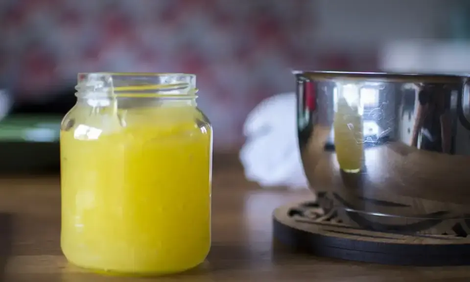 En burk med hemgjord lemon curd står bredvid en metallskål.
