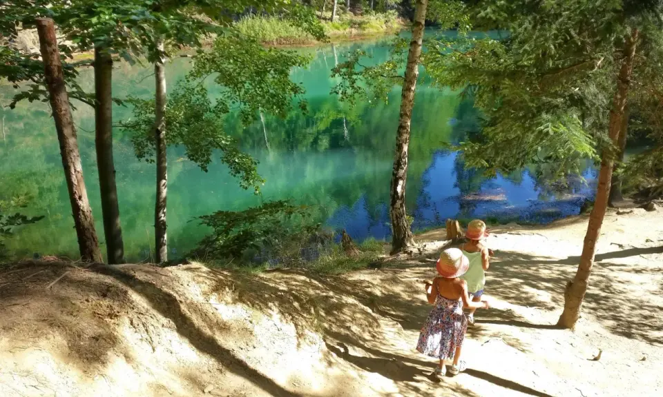 Dwie dziewczynki w słomkowych kapeluszach spacerują ścieżką nad turkusowym jeziorem. Idealne miejsce, gdzie w góry z dziećmi na Śląsku.