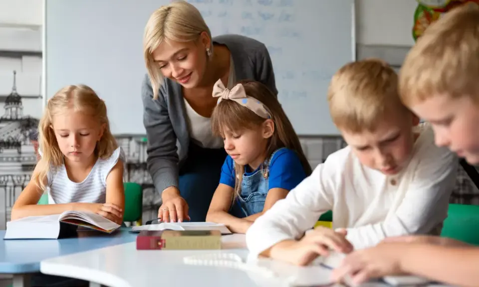 Nauczycielka, jak dobry oligofrenopedagog, wspiera dzieci w nauce przy stolikach.