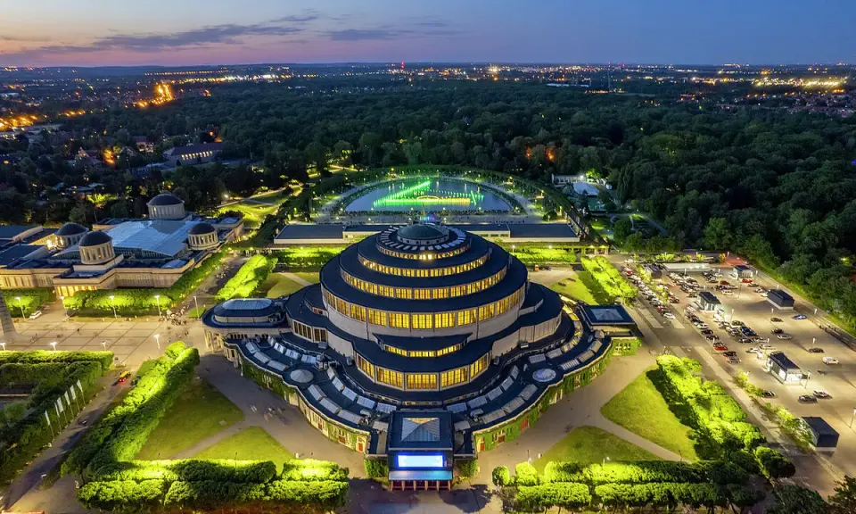 Wrocław Hala Stulecia nocą, z podświetloną fontanną i otaczającym parkiem.