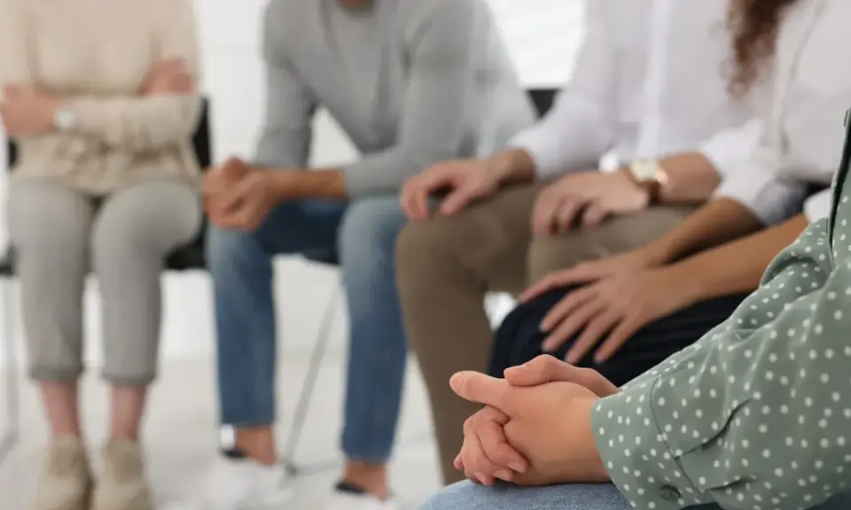 Grupa osób siedzi w kręgu, wspierając się nawzajem. To obraz nadziei i wspólnej drogi w terapii od uzależnień.