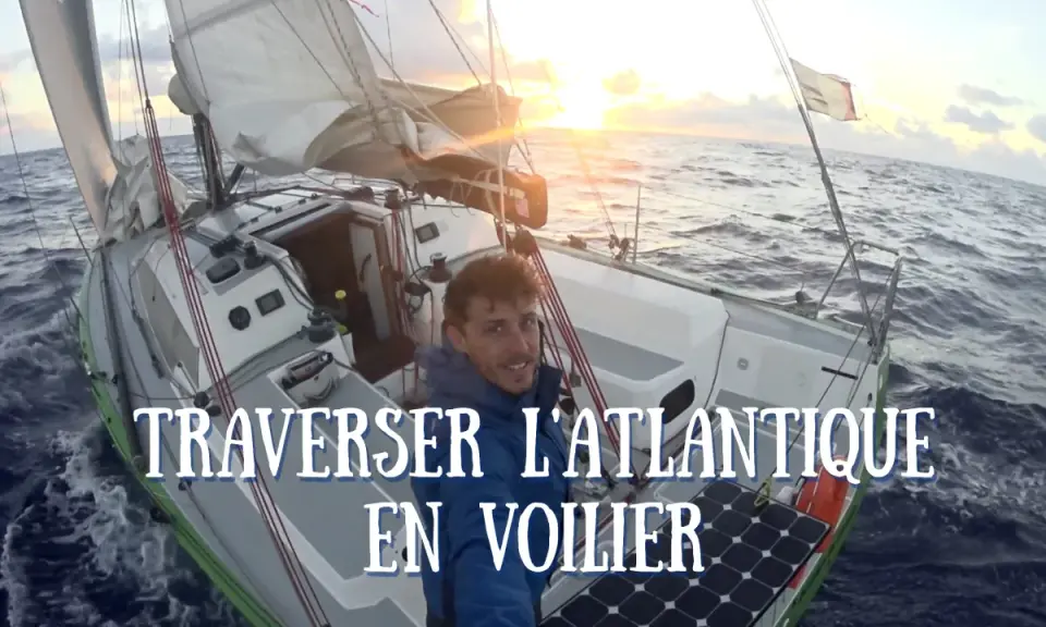 Un homme souriant sur un voilier en pleine traversée de l'Atlantique. Le soleil se lève, illuminant les voiles. Quel voilier pour traverser l'Atlantique ? Celui-ci semble parfait.