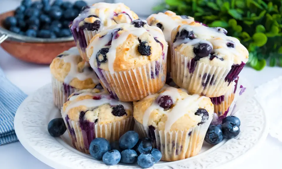 Stosik pysznych muffinek z borówkami, polanych lukrem, ozdobiony świeżymi owocami.
