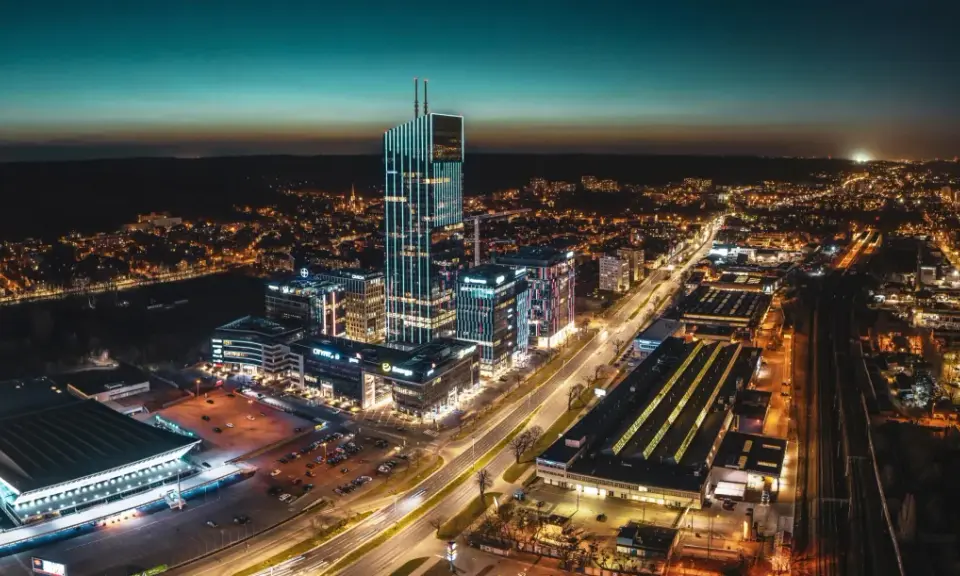 Widok z lotu ptaka na nowoczesne centrum miasta nocą, z oświetlonymi wieżowcami i ulicami.