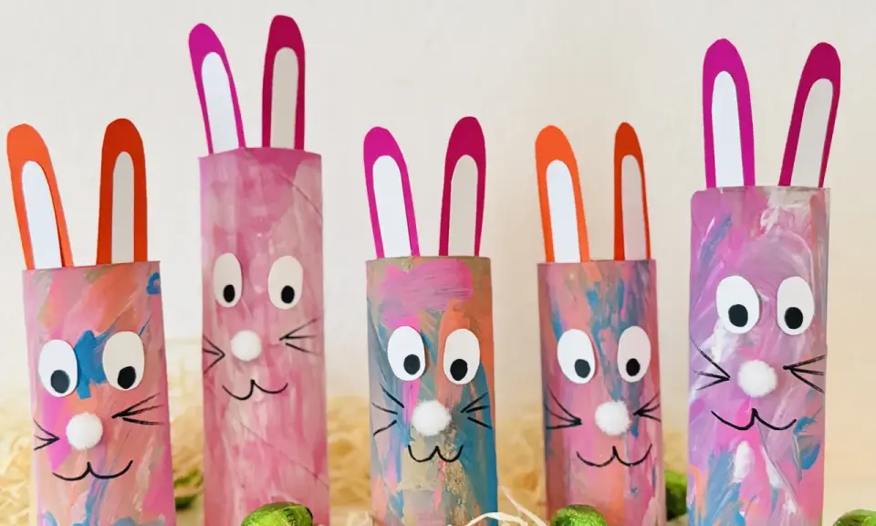 Fünf bunte Osterhasen aus Klopapierrollen mit großen Augen und rosa Ohren, dekoriert mit Pinselstrichen.