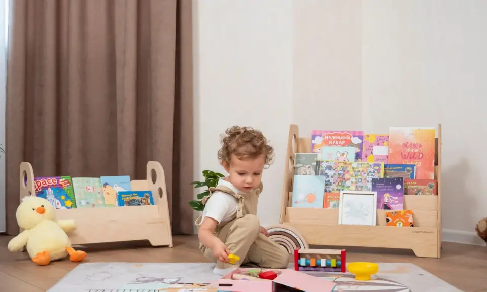 Kleines Kind spielt mit Holzspielzeug vor einem Regal mit Büchern, das eine Sitzordnung im Montessori-Stil widerspiegelt.