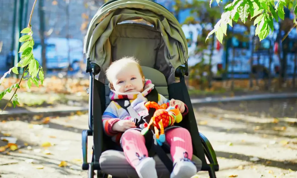 Uśmiechnięte dziecko w wózku, trzymające kolorową zabawkę. Czas na spacer, do kiedy gondola posłuży maluchowi?