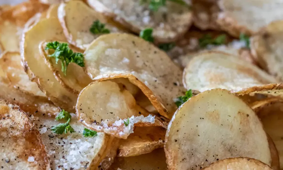 Krispiga, gyllene skivor av friterad potatis, strödda med salt och peppar, toppade med färsk persilja.