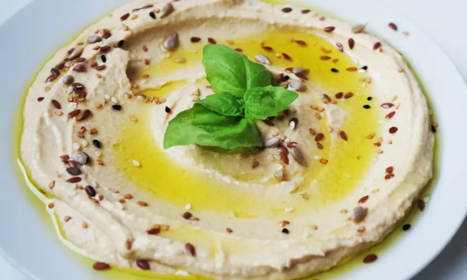 Cremiger Hummus, garniert mit Öl, Kräutern und Samen. Tahin ist die geheime Zutat für diese köstliche Dip-Kreation.