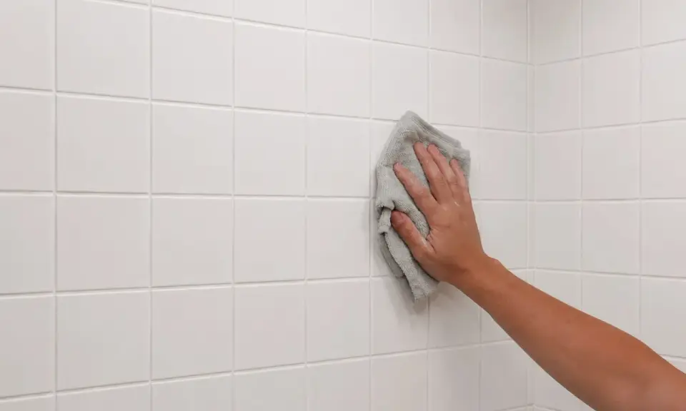 Mano limpiando azulejos blancos recién colocados con un paño gris.