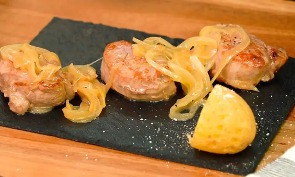Tiernos medallones de carne al jerez, cubiertos con cebolla caramelizada y acompañados de una porción de patata.
