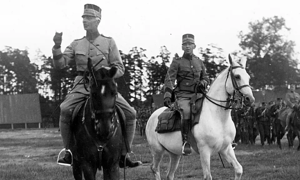 Två militärer till häst, kanske under en övning för regementen i Sverige. Bakom syns fler soldater och träd.