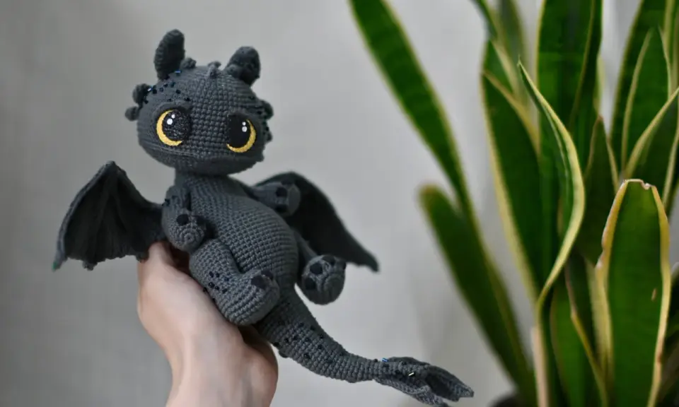 Adorable dragón amigurumi gris con ojos amarillos brillantes. ¡Encuentra el dragon amigurumi patron gratis en español para crear el tuyo!