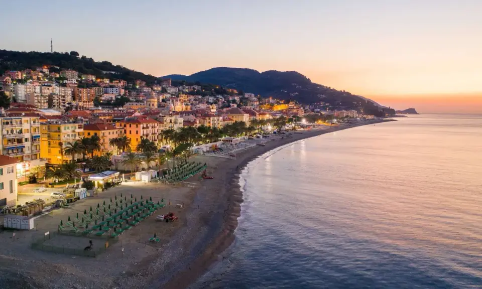 Alba sulla spiaggia finale ligure, con file di ombrelloni verdi e palme che si affacciano sul mare calmo.