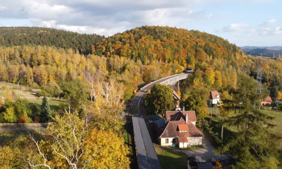 Jesienna panorama Gór Sowich. Widok na most kolejowy, tory i domy wśród kolorowych drzew. Atrakcje turystyczne regionu.