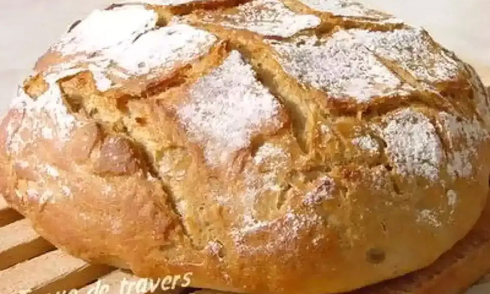 Gros pain artisanal, saupoudré de farine, avec une croûte dorée et des incisions. Ce pain farine de chataigne semble tout juste sorti du four.