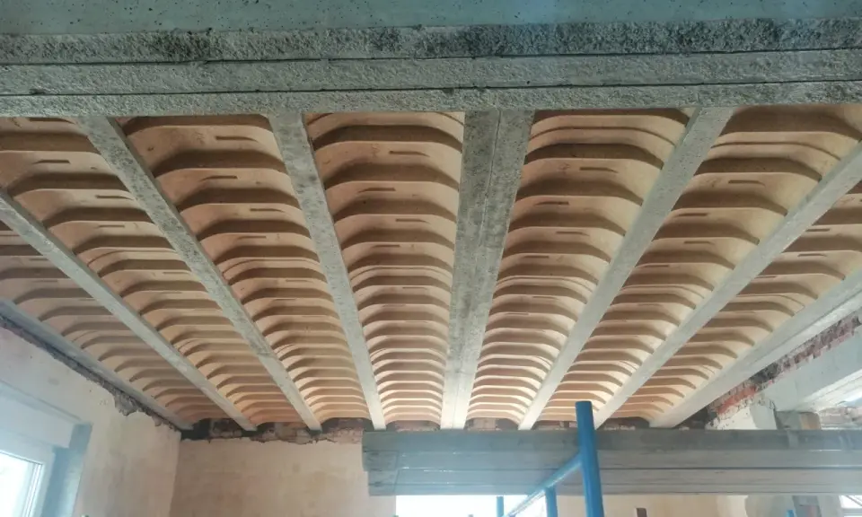 Widok od dołu na betonowe belki stropowe i pustaki ceramiczne, ukazujące różne rodzaje stropów w trakcie budowy.
