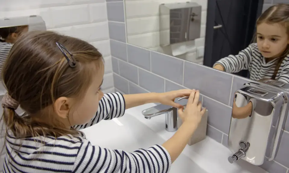 Niña se lava las manos en el baño, un gesto importante para la higiene y la prevención del toc en niños.