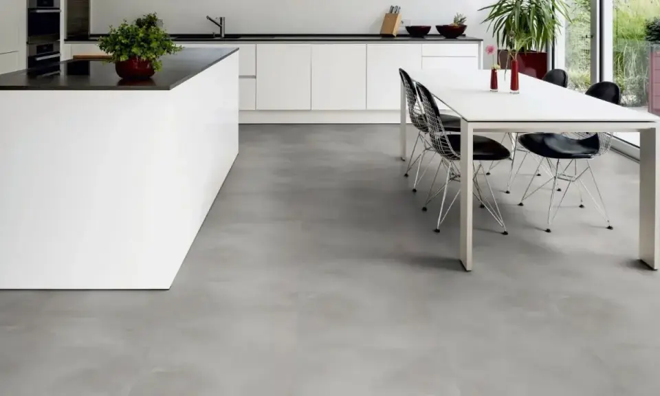 Cucina moderna con isola bianca e tavolo da pranzo. Il pavimento in LVT grigio effetto cemento completa l'ambiente minimalista.