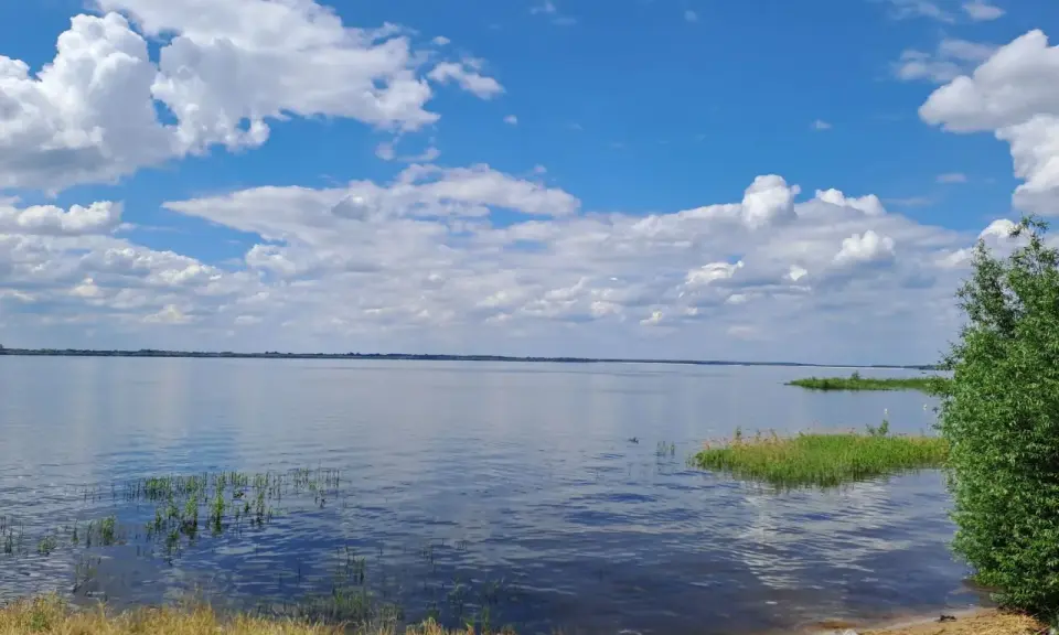 Spokojny zalew Jeziorsko w letni dzień. Błękitne niebo z białymi chmurami odbija się w tafli wody.