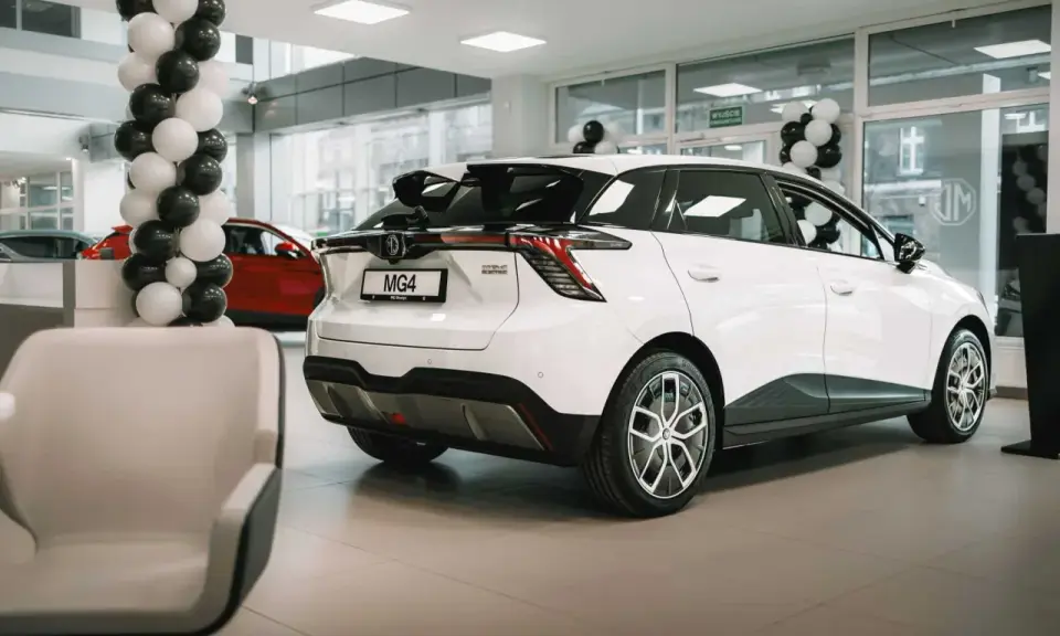 Białe auto MG 4 Electric w salonie, ozdobionym balonami. Obok czerwony samochód i wygodne fotele.