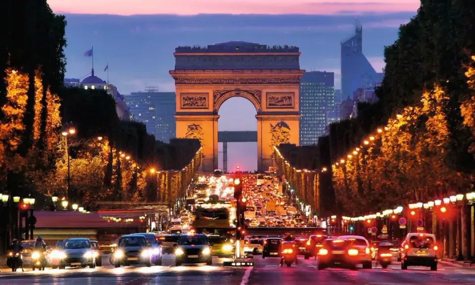 Trafikkaos vid Triumfbågen i Paris. En kvällspromenad här känns som att bada i Paris ljus.