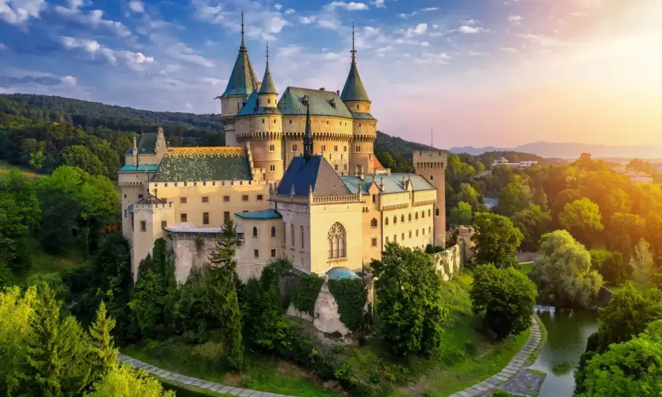 Bajkowy zamek otoczony zielenią, niczym zamek hotel w Polsce, zachwyca o zachodzie słońca.