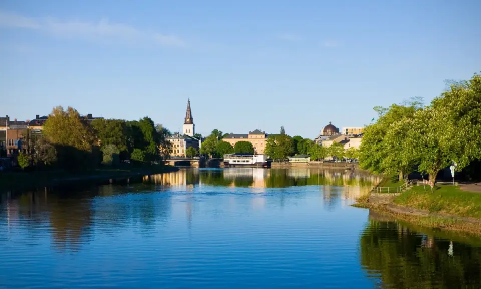 Vacker vy över Klarälven i Karlstad med stadens silhuett och grönska. Perfekt för promenader och andra aktiviteter Karlstad erbjuder.
