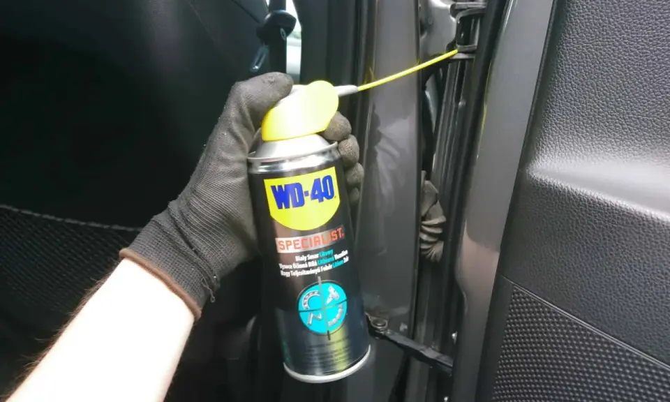 Ręka w rękawiczce aplikuje smar do zawiasów drzwi samochodowych WD-40 Specialist.