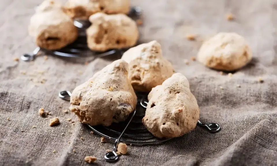 Biscotti meringati, dall'aspetto rustico ma dal sapore delizioso, noti come "brutti ma buoni", su una griglia.