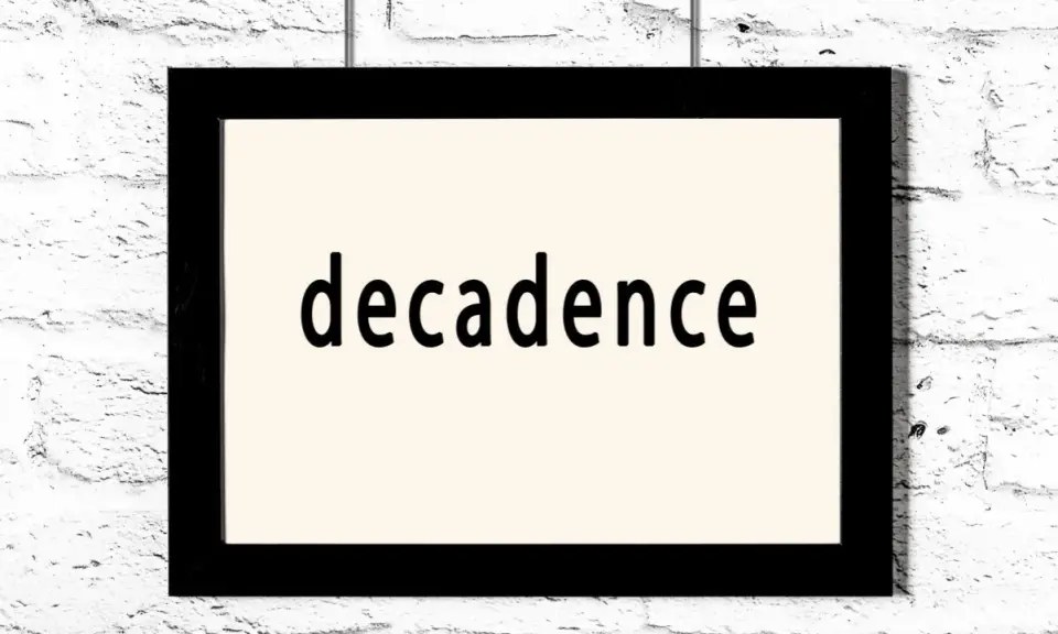 Czarny prostokątny obraz z napisem "decadence" na jasnym tle, wiszący na białej ceglanej ścianie. Symbol dekadentyzmu.